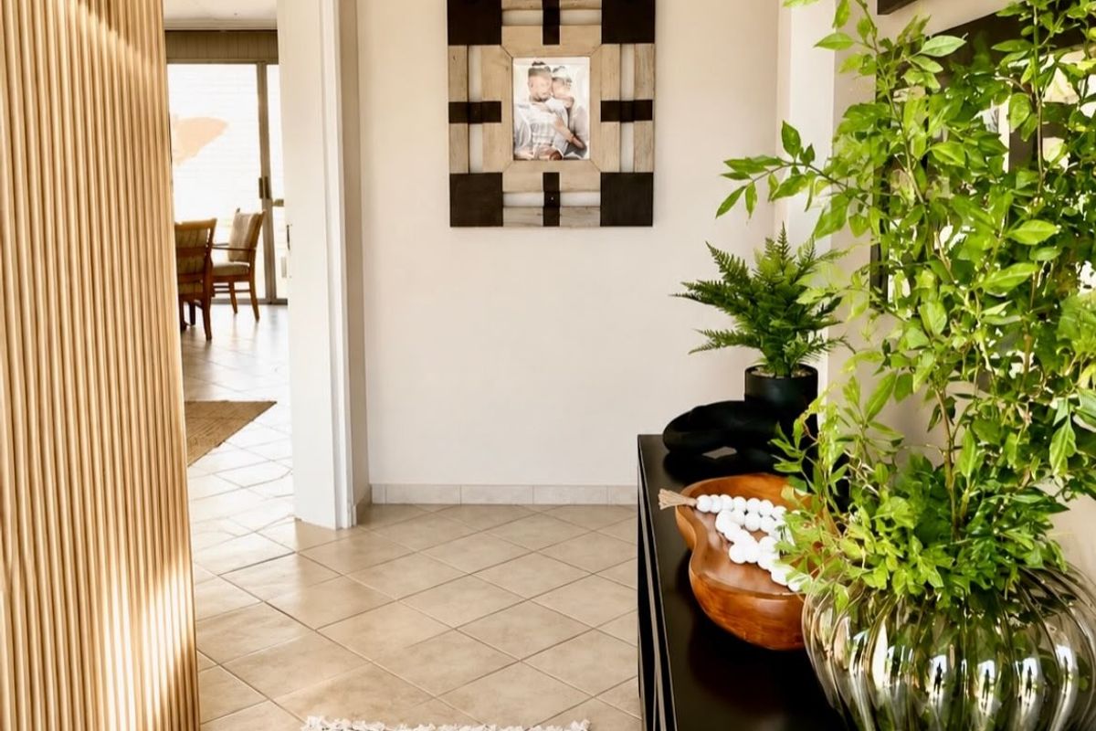A bright and welcoming entrance hall featuring neutral tiled flooring and a decorative slatted timber room divider leading into the main living area.