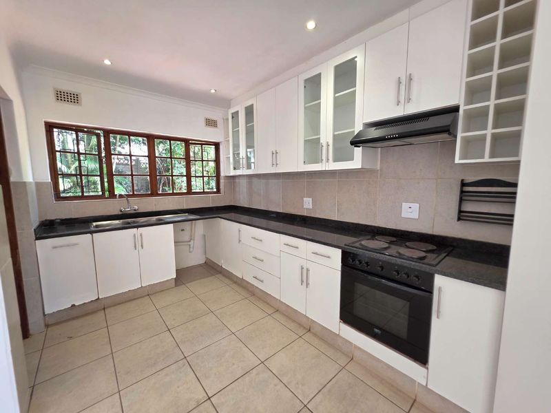 A clean, functional kitchen featuring white cabinetry, granite countertops, built-in oven and hob, and tiled flooring with ample natural light.