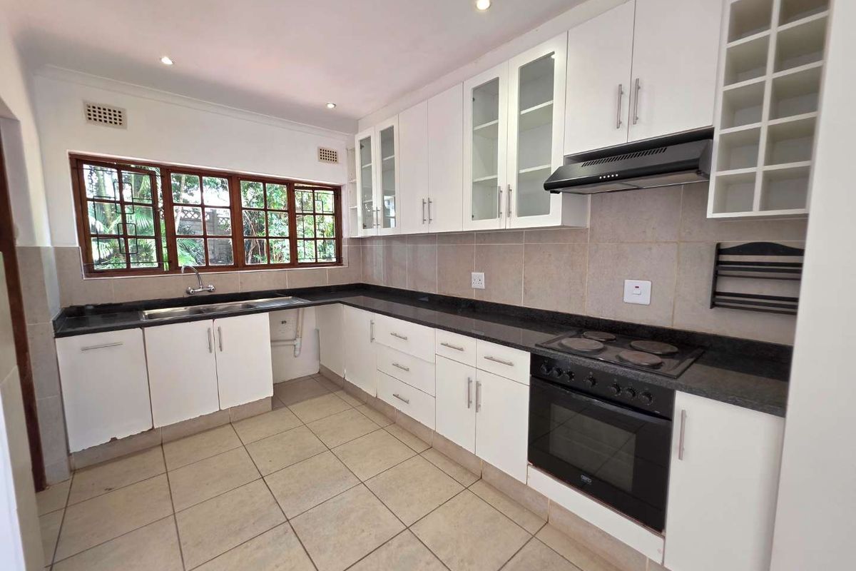 A clean, functional kitchen featuring white cabinetry, granite countertops, built-in oven and hob, and tiled flooring with ample natural light.