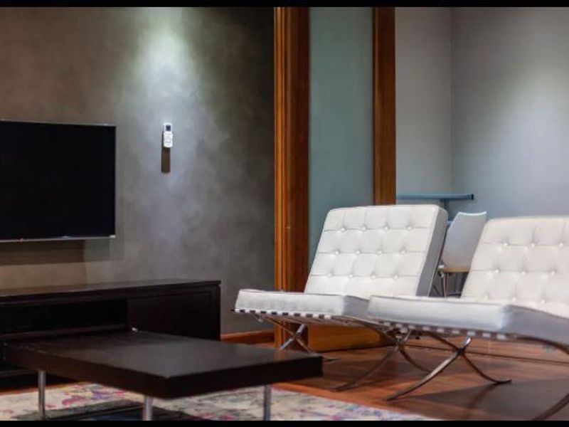 A modern living room featuring hardwood flooring, a feature wall with a wall-mounted television, and a sliding glass door leading to an adjacent space.
