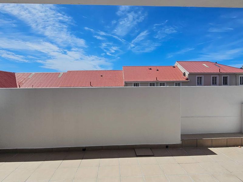 An open-air balcony featuring tiled flooring and a solid parapet wall, offering an unobstructed view of the surrounding neighborhood rooftops.