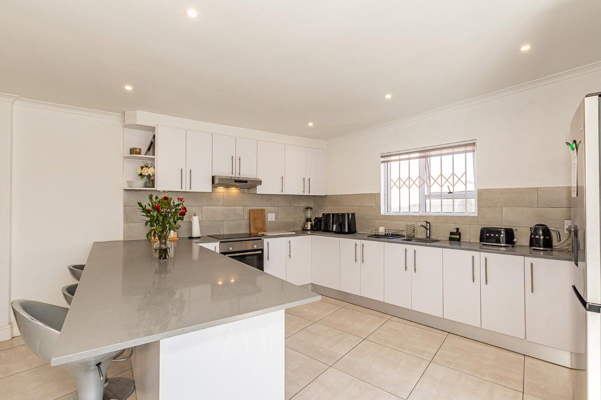 Modern kitchen featuring white cabinetry, stone countertops, a breakfast bar, integrated oven, extractor fan, and tiled flooring.