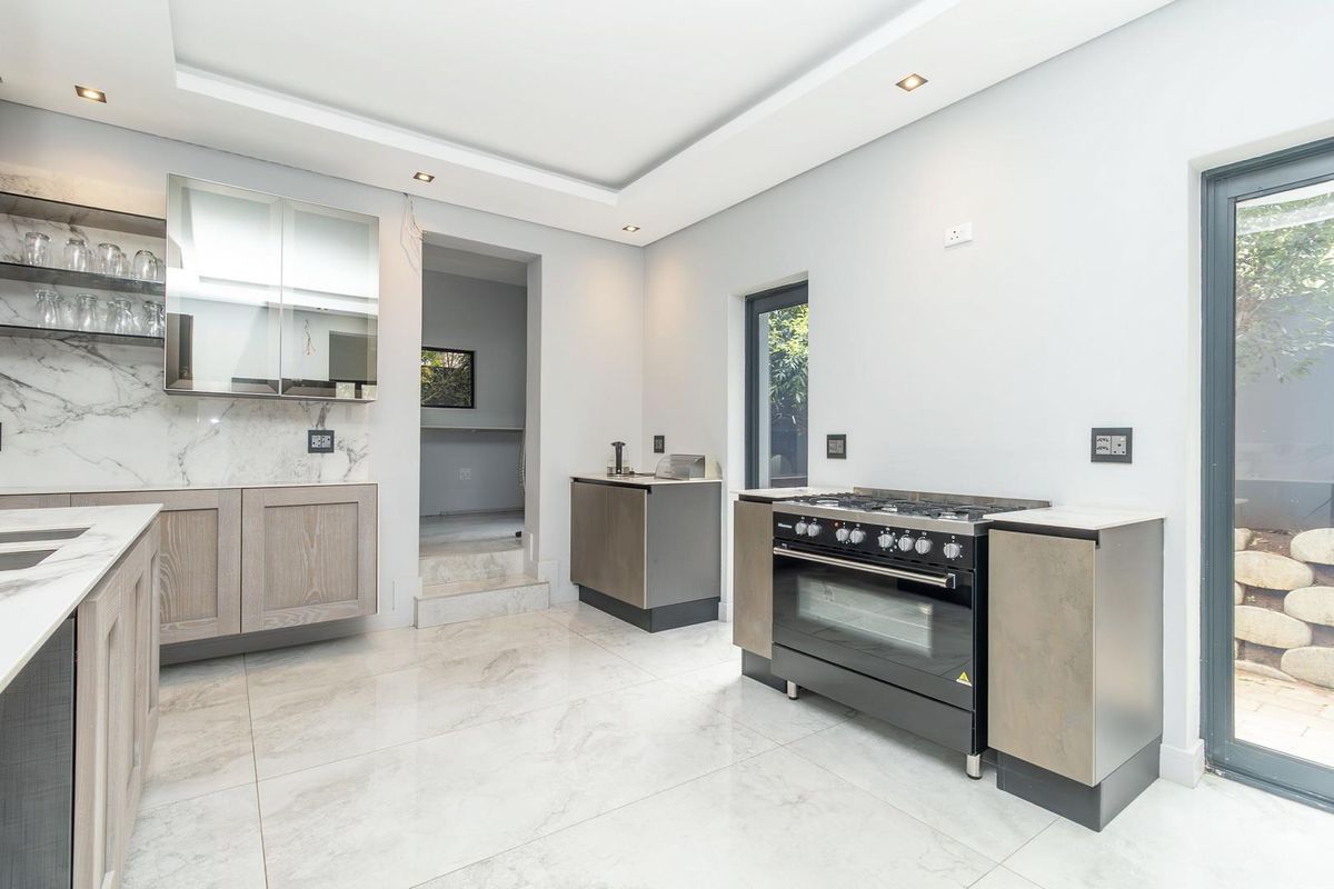 Modern kitchen featuring marble-look tiled flooring, stone splashbacks, sleek cabinetry, and a freestanding gas stove with oven.