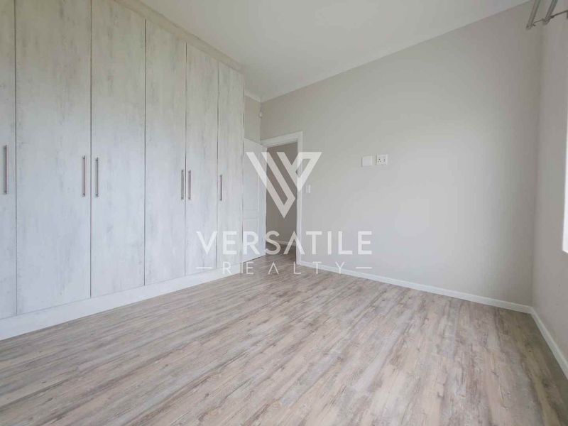 A bright, empty bedroom featuring modern light-toned laminate flooring and extensive built-in cupboard storage.