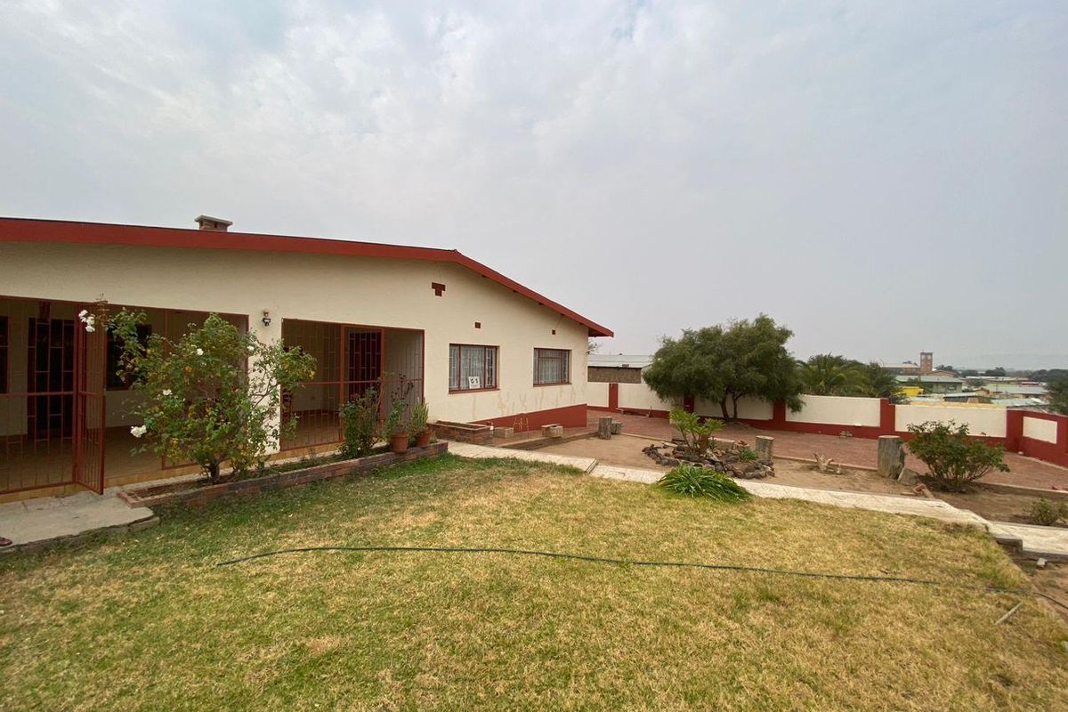 Rear view of the property featuring a covered patio, established garden, and perimeter boundary wall.