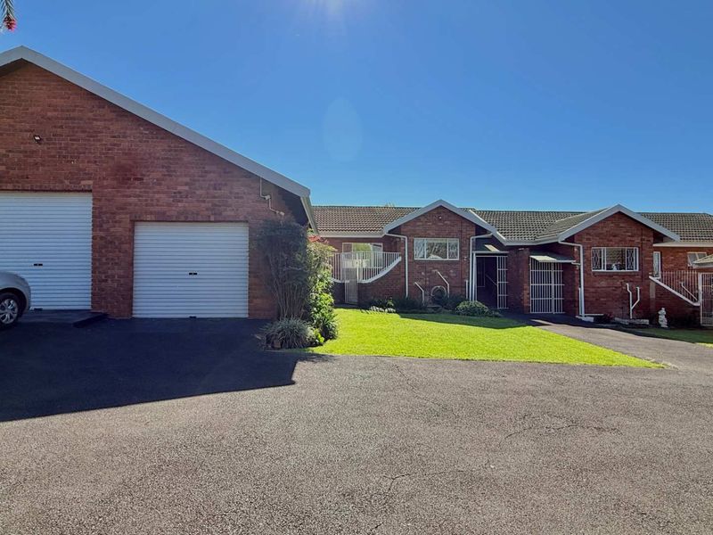Front view of a brick townhouse featuring a double garage, paved driveway, and a well-maintained front lawn.