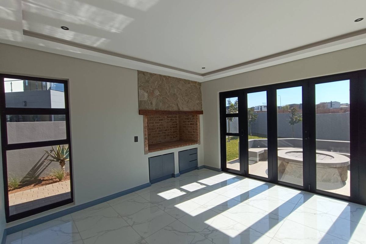 Bright living area featuring large aluminium stack doors opening to the patio, built-in braai with stone cladding, and modern marble-look tiled flooring.