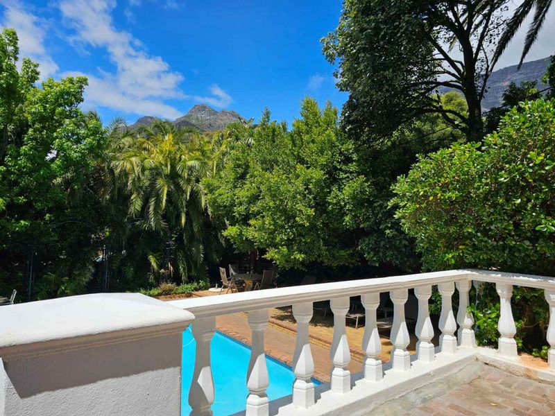 Outdoor pool area featuring a classic white balustrade, brick paving, and lush garden surroundings with mountain views.