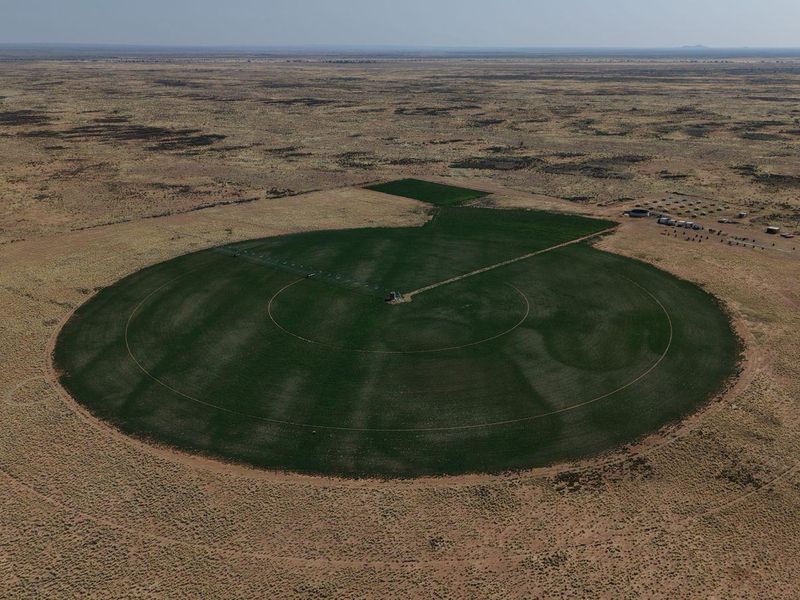 Aerial view of a large-scale farm featuring a circular crop field managed by a center pivot irrigation system in an arid landscape.