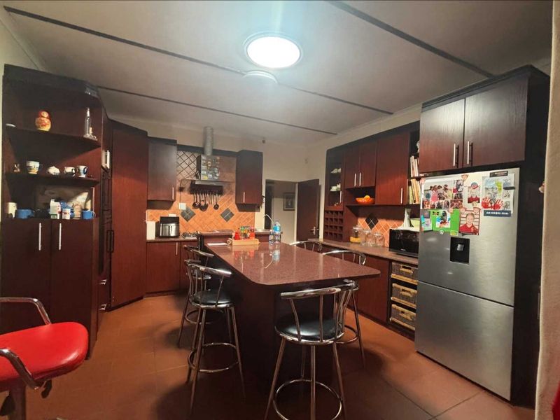 A spacious kitchen featuring dark wood cabinetry, a central island with stone countertops, tiled backsplash, and tiled flooring.