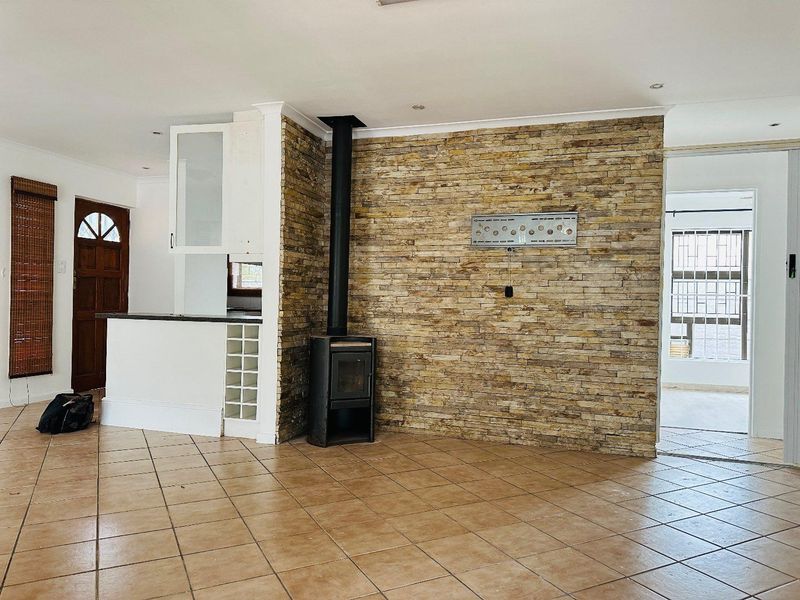 Spacious living area featuring a prominent stone feature wall, a freestanding fireplace, and neutral ceramic floor tiles throughout.