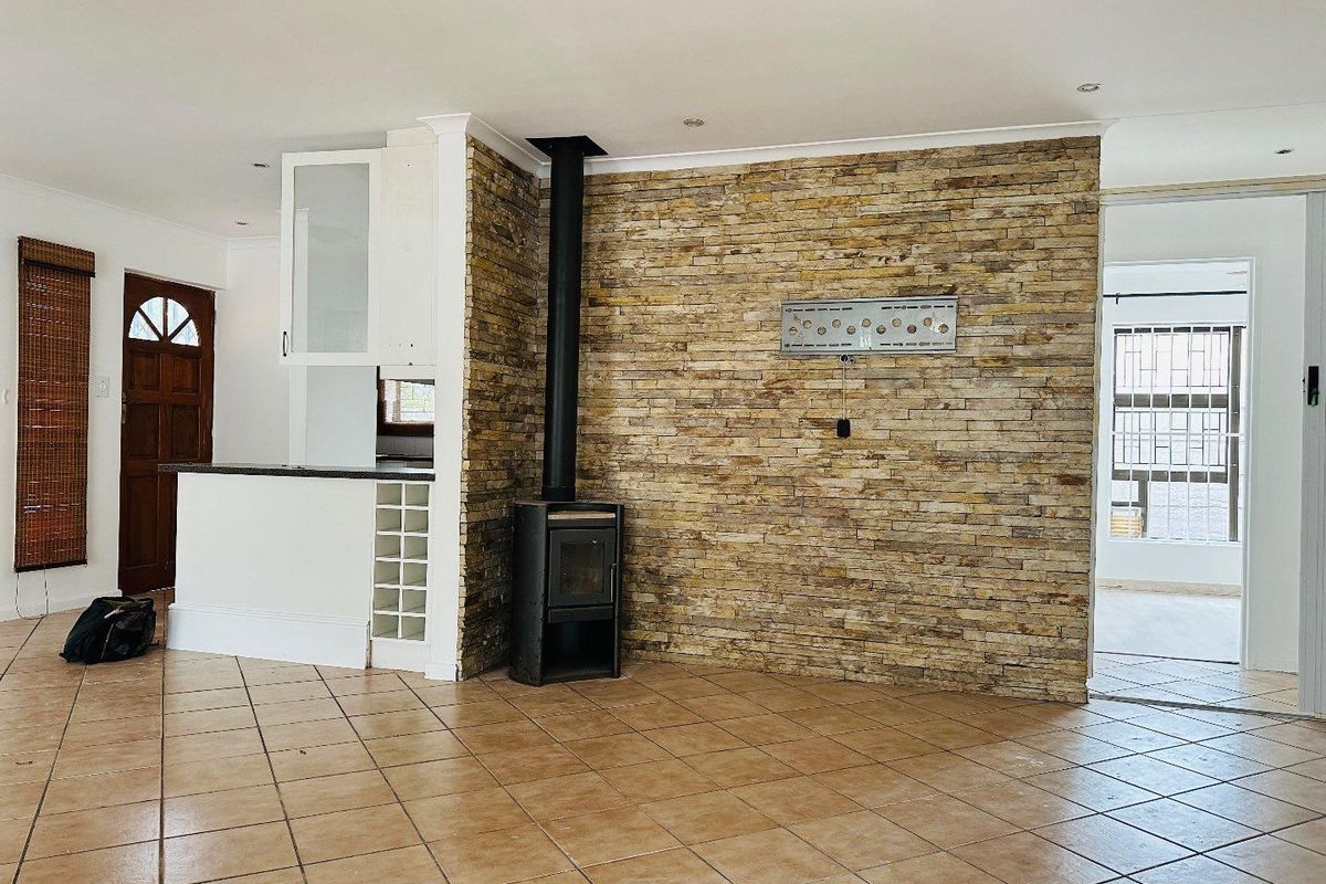 Spacious living area featuring a prominent stone feature wall, a freestanding fireplace, and neutral ceramic floor tiles throughout.