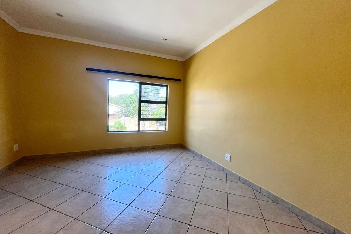 A bright, empty bedroom featuring neutral tiled flooring, recessed downlighting, and security bars on the window.