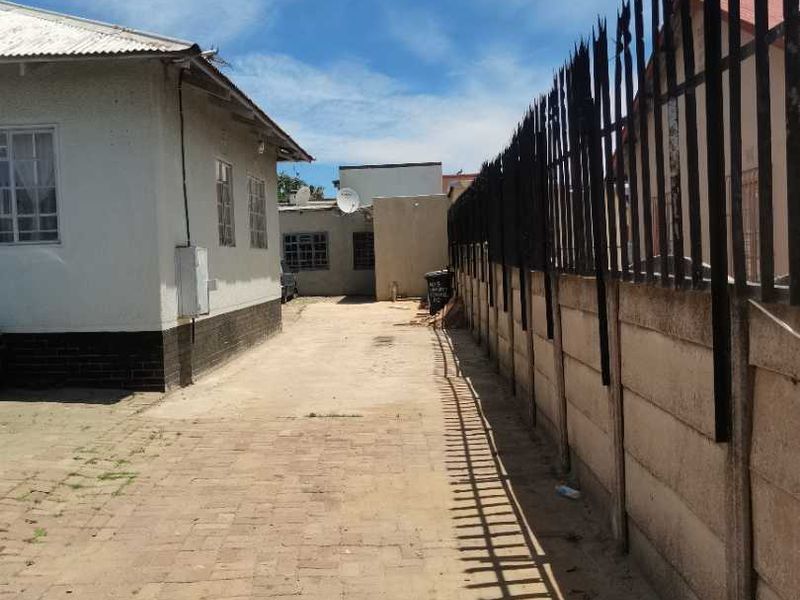 A side exterior view showing a paved driveway, a precast concrete boundary wall with security spikes, and the side elevation of the house.