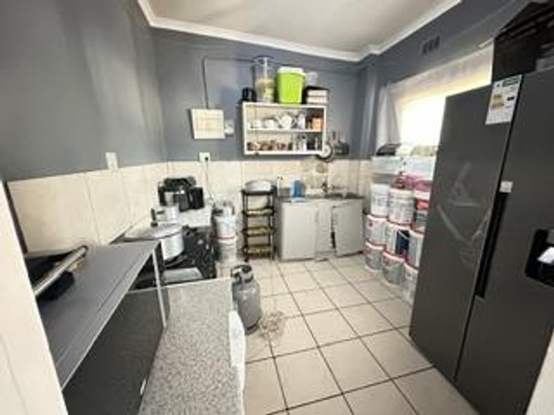 A functional scullery area featuring tiled flooring, a built-in sink, tiled splashbacks, and wall-mounted storage shelving.