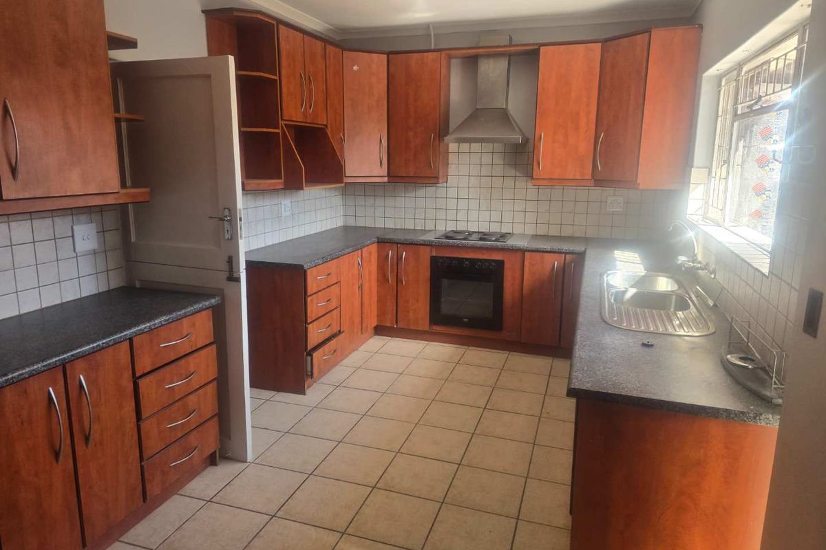 A functional kitchen featuring wood-finish cabinetry, dark laminate countertops, a built-in oven, extractor fan, and tiled flooring with a double-basin sink.