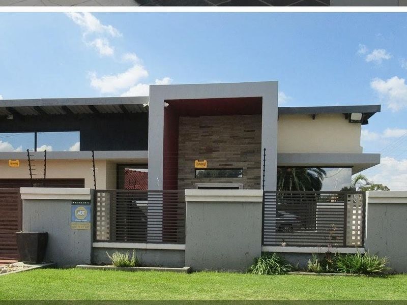 Modern contemporary front facade featuring stone cladding, clean architectural lines, secure boundary wall with electric fencing, and a well-maintained front lawn.