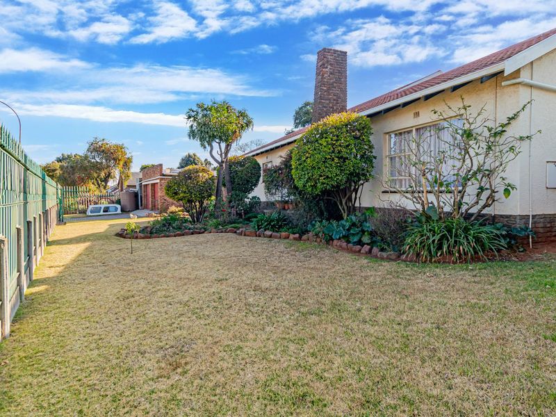 A view of the rear exterior of the house featuring a brick chimney, tiled roof, and a fenced garden area.