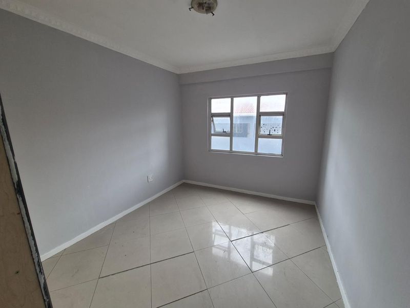 A clean, empty bedroom featuring neutral grey walls, tiled flooring, and a large window providing natural light.