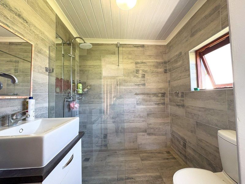 Modern bathroom featuring a spacious walk-in shower with glass screen, contemporary vanity basin, and neutral wood-look wall and floor tiling.
