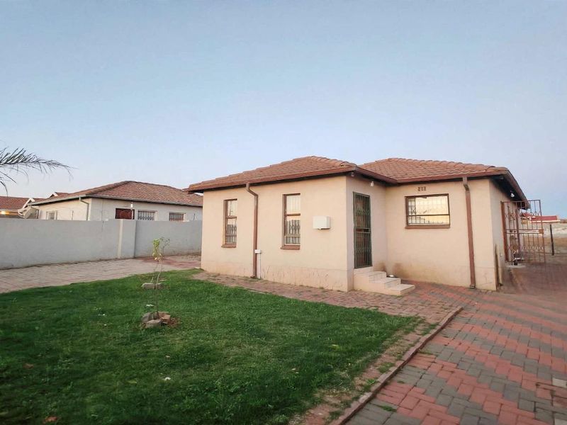 Rear view of a detached house featuring a tiled roof, paved driveway, and enclosed garden area with boundary walls.