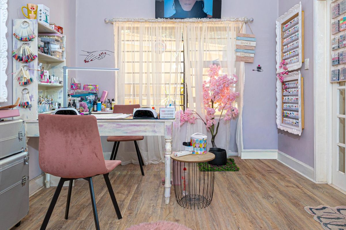 A functional room currently utilized as a beauty workspace, featuring wood-look flooring, neutral wall finishes, and a window with sheer curtains.