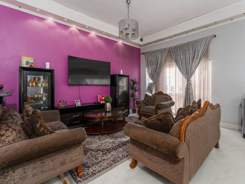 A living room featuring a bold accent wall, recessed ceiling lighting, and crown molding, with a visible structural crack near the window area.