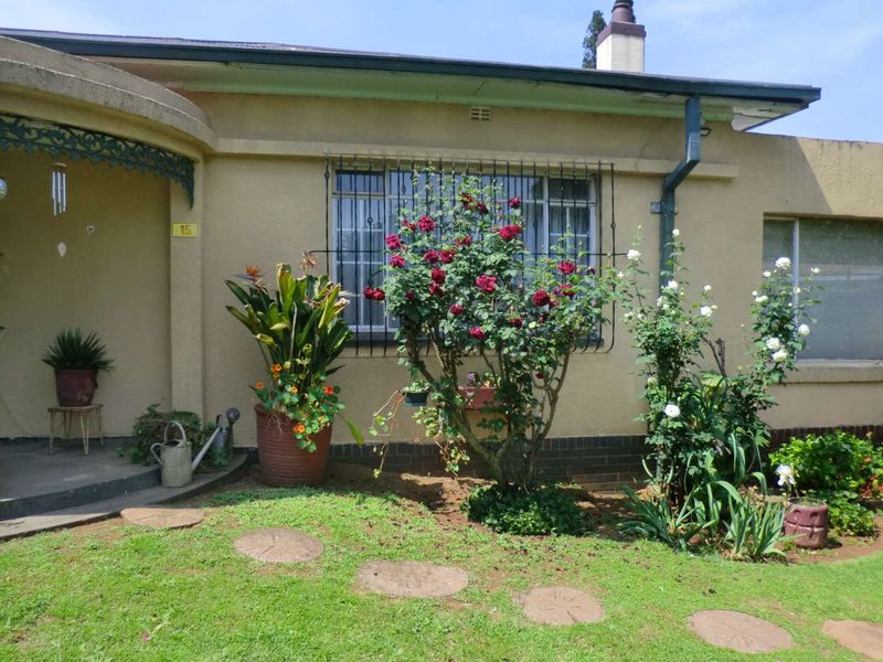 Front facade of a residential home featuring a concrete porch, security bars on windows, and established garden beds.