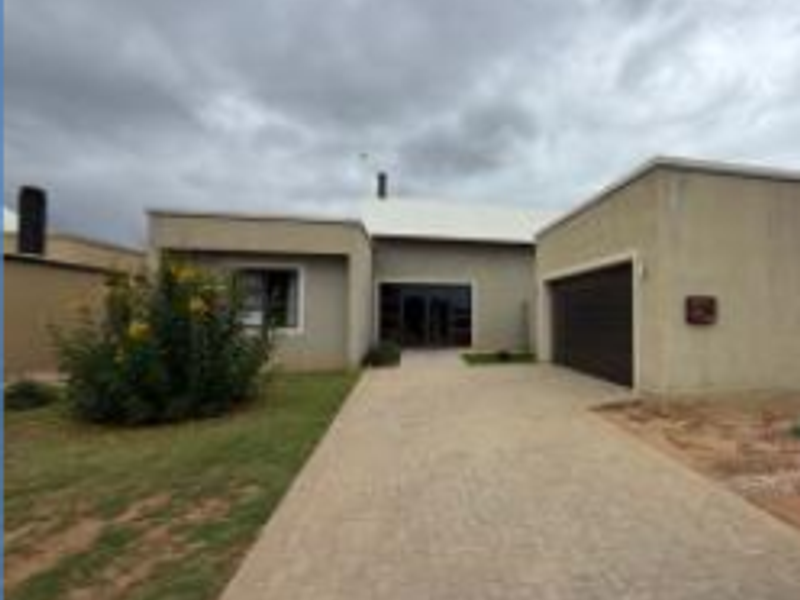 Front elevation of a single-story house featuring a paved driveway, integrated garage, and a central entrance under a cloudy sky.