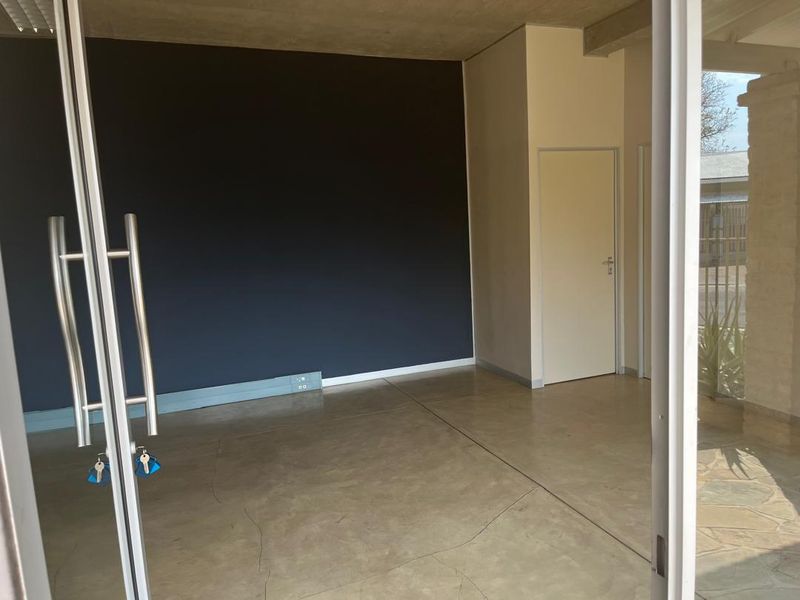 A vacant office space featuring polished concrete flooring, a dark accent wall, and modern glass double door entry.