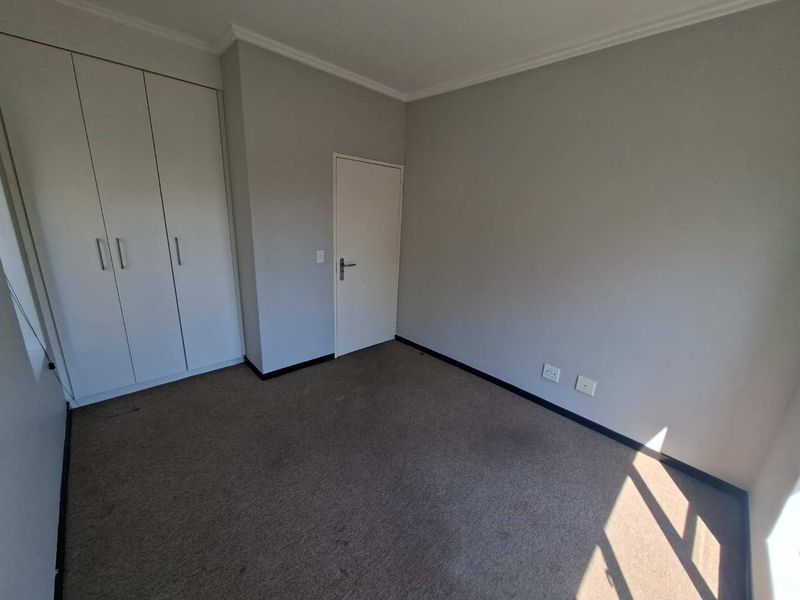 An empty bedroom featuring neutral wall paint, carpeted flooring, and built-in cupboards, providing a clean and versatile space ready for personalization.
