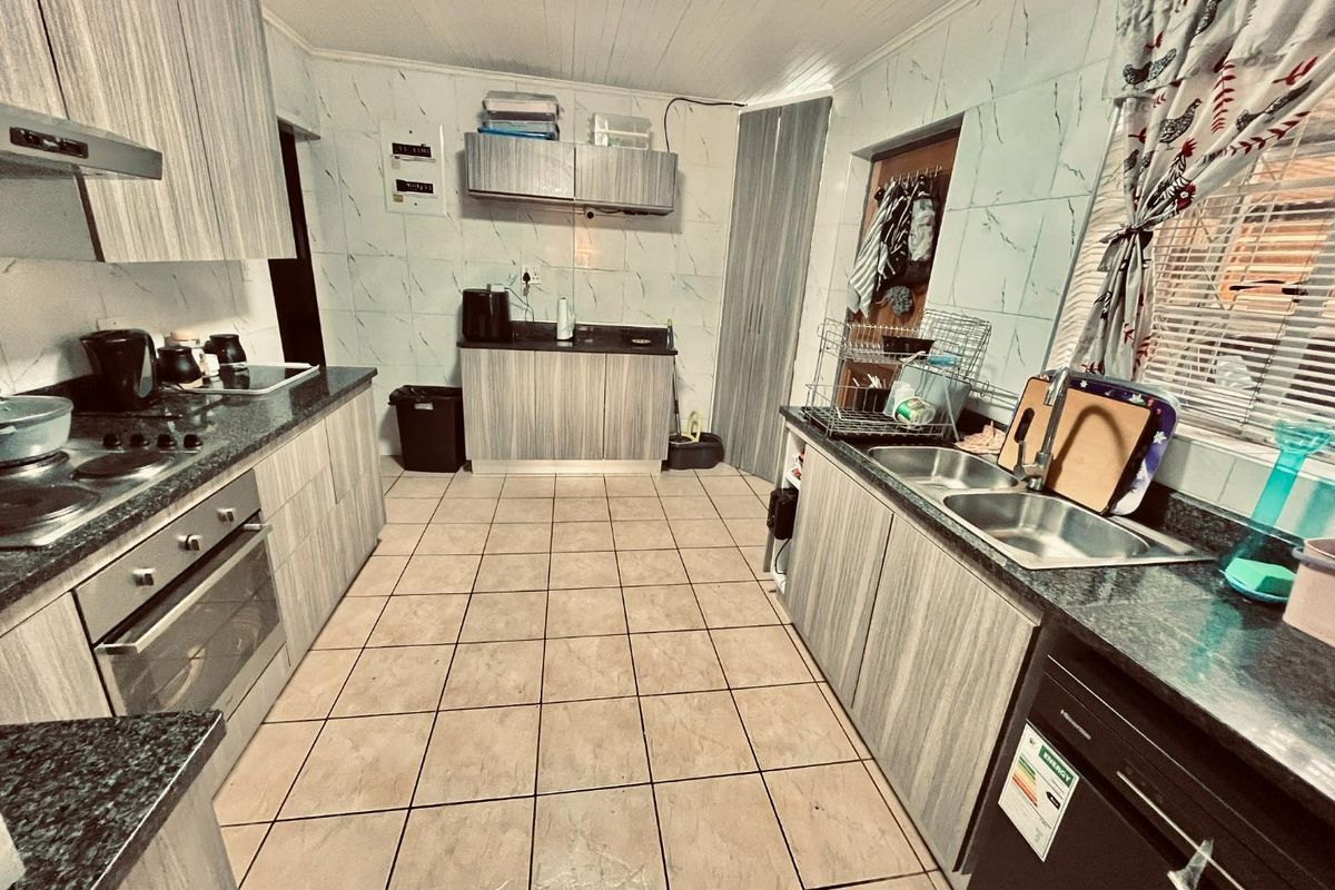 A functional kitchen featuring wood-grain cabinetry, granite-look countertops, a built-in oven and hob, and tiled flooring throughout.