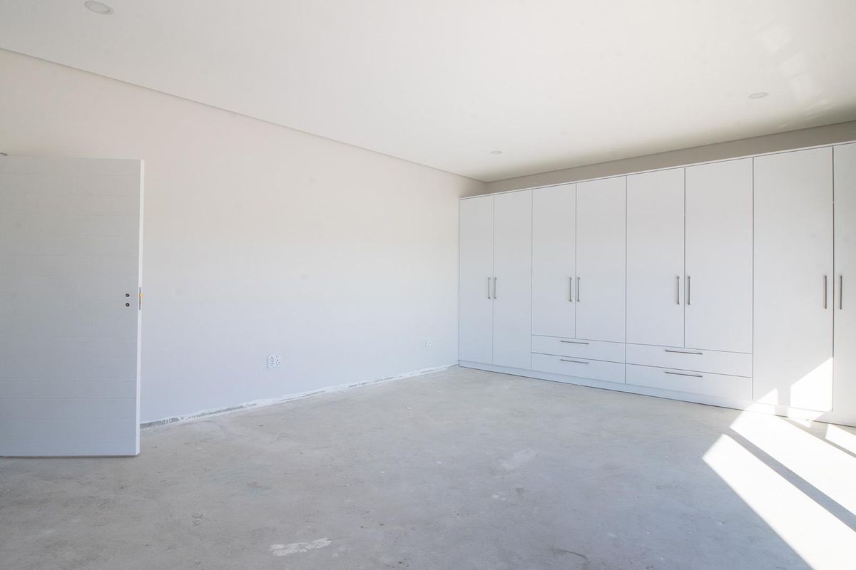 A spacious, empty bedroom featuring extensive built-in white cabinetry and a neutral color palette, ready for final flooring installation.