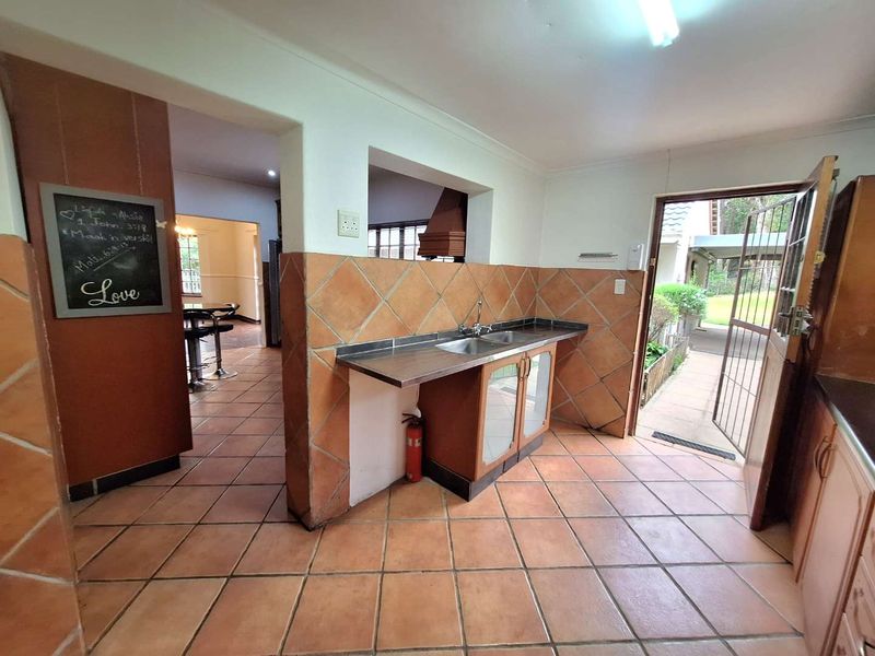 A functional scullery area featuring tiled flooring, a double stainless steel sink, and direct access to the exterior garden.