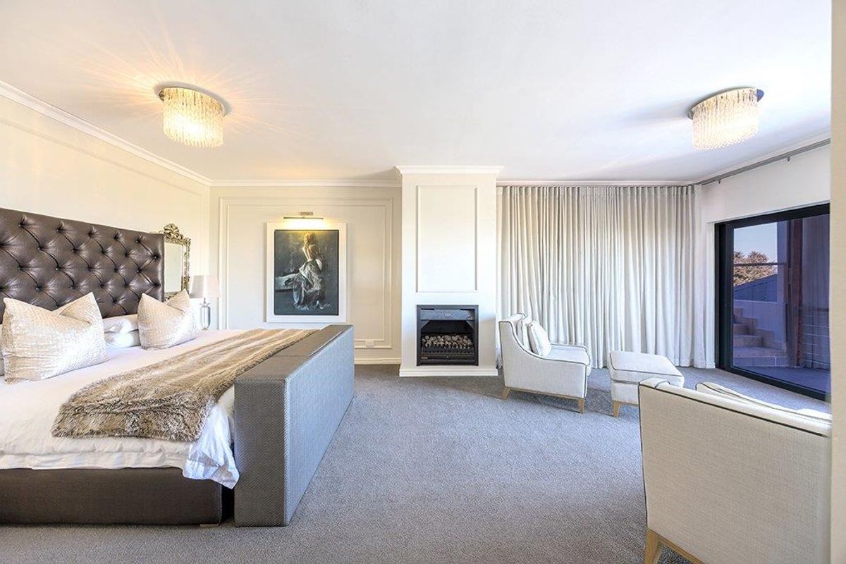 Spacious master bedroom featuring a built-in fireplace, elegant wall molding, plush carpeting, and large sliding glass doors leading to an outdoor area.