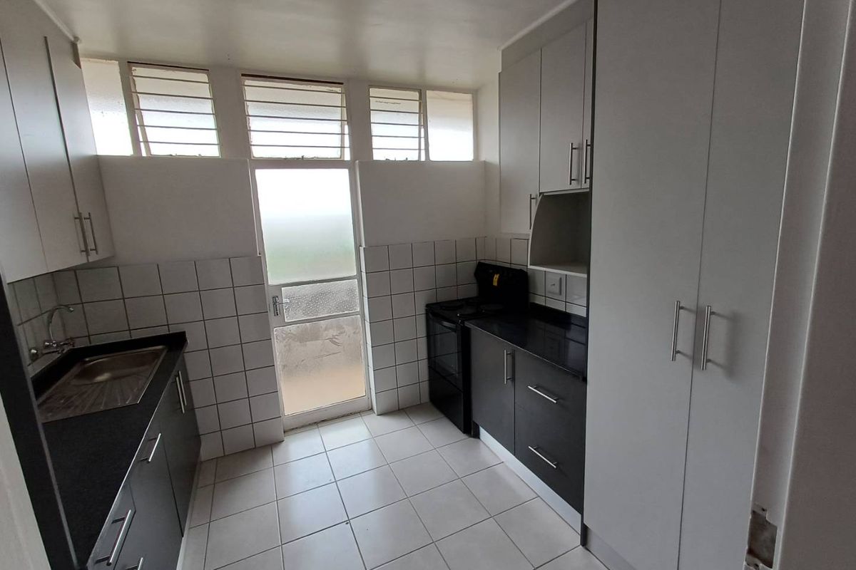 A functional kitchen featuring dark cabinetry, contrasting countertops, tiled backsplash, and direct access to an outdoor area through a glass panel door.
