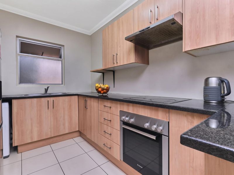 A functional kitchen featuring light wood-finish cabinetry, dark granite countertops, built-in oven, electric hob, and tiled flooring.
