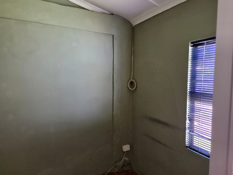 An empty room featuring olive-toned walls, venetian blinds, and visible electrical infrastructure requiring maintenance and cosmetic updates.