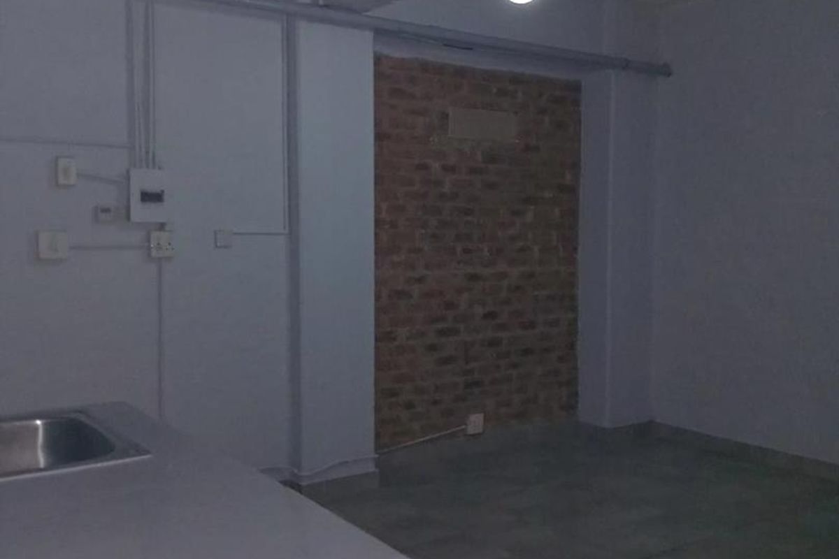 An empty, industrial-style kitchen area featuring exposed brickwork, tiled flooring, and exposed electrical conduit, offering a blank canvas for renovation.