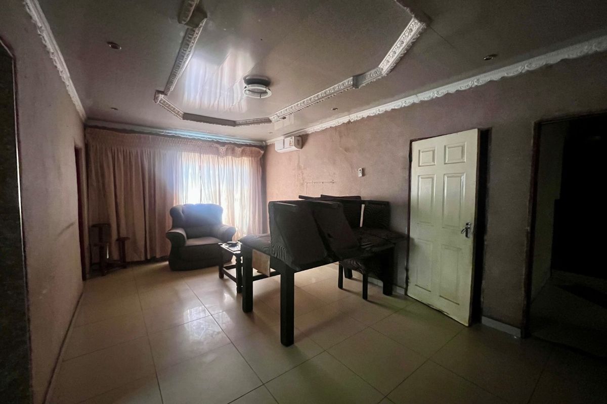 A living room featuring tiled flooring, decorative ceiling molding, and an air conditioning unit, requiring cosmetic updates to improve the overall aesthetic.