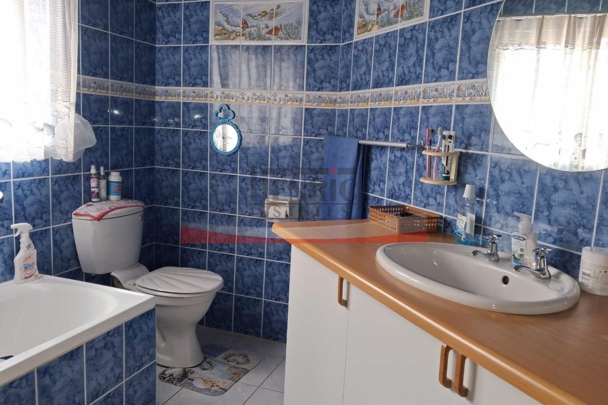 A functional bathroom featuring blue tiled walls, a built-in vanity with a ceramic basin, a toilet, and a bathtub.