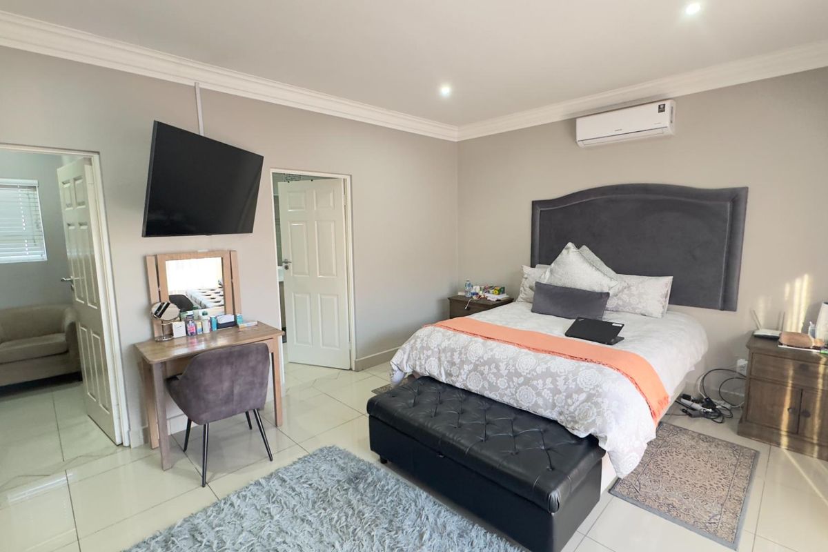 Spacious bedroom featuring tiled flooring, crown molding, a wall-mounted air conditioning unit, and direct access to an adjoining room.