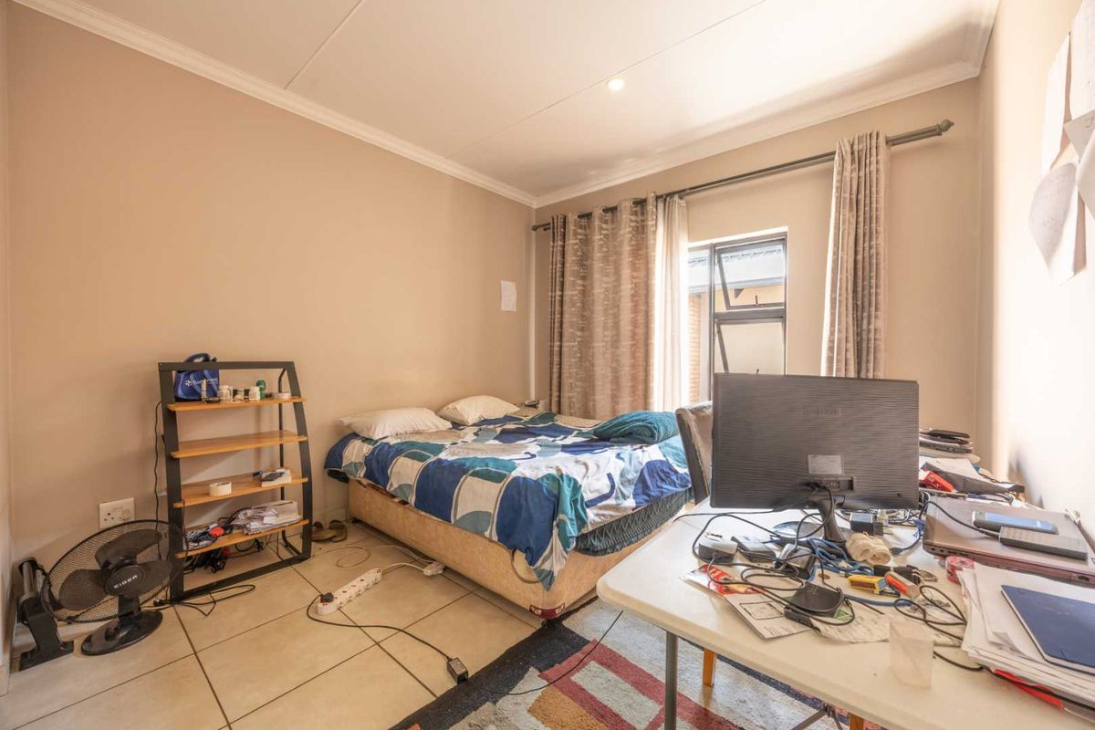 A functional bedroom featuring tiled flooring, coved ceilings, and an aluminium-framed window, providing a neutral base for potential interior updates.