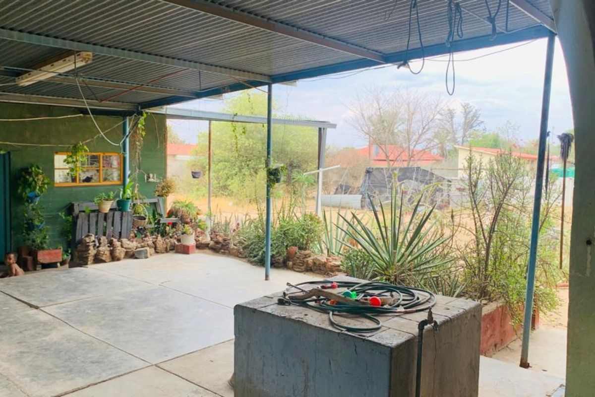 A covered outdoor patio area featuring a corrugated metal roof, concrete flooring, and a built-in concrete plinth with an outdoor water tap.