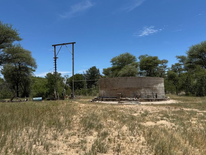 An outdoor utility area on the farm featuring a large concrete water reservoir and a borehole pump structure set in a natural landscape.