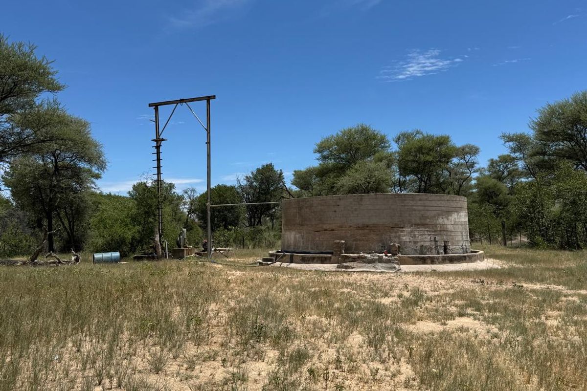 An outdoor utility area on the farm featuring a large concrete water reservoir and a borehole pump structure set in a natural landscape.