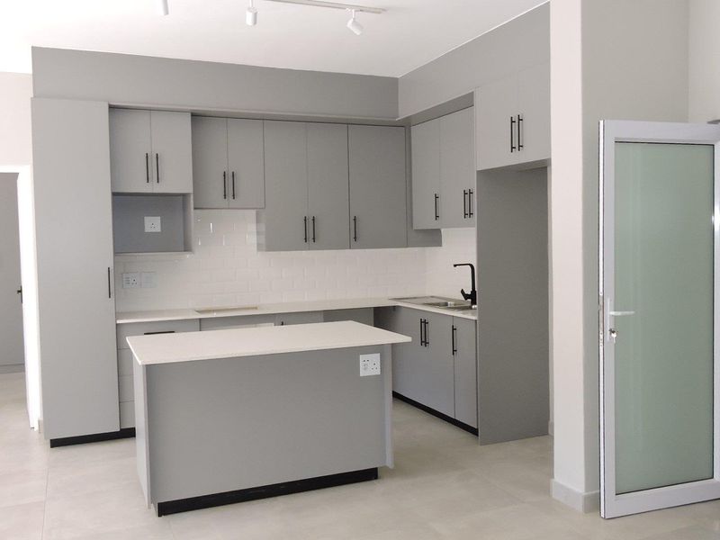 Modern kitchen featuring grey built-in cabinetry, a central island, white subway tile backsplash, quartz countertops, and a sleek matte black faucet.
