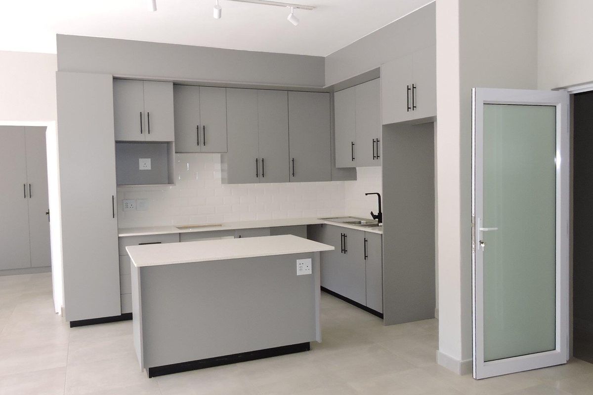 Modern kitchen featuring grey built-in cabinetry, a central island, white subway tile backsplash, quartz countertops, and a sleek matte black faucet.