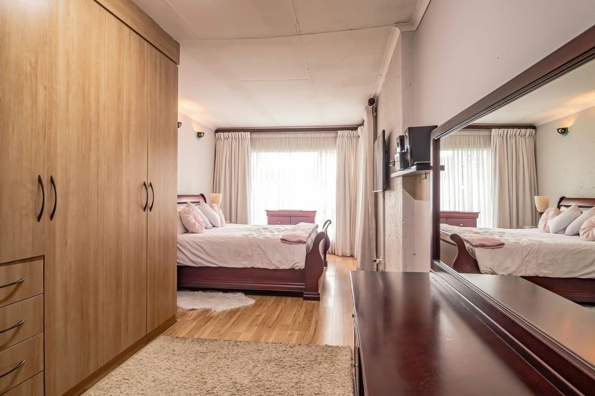 Spacious bedroom featuring light wood-tone built-in wardrobes, laminate flooring, and large windows with curtains, creating a bright and comfortable living space.