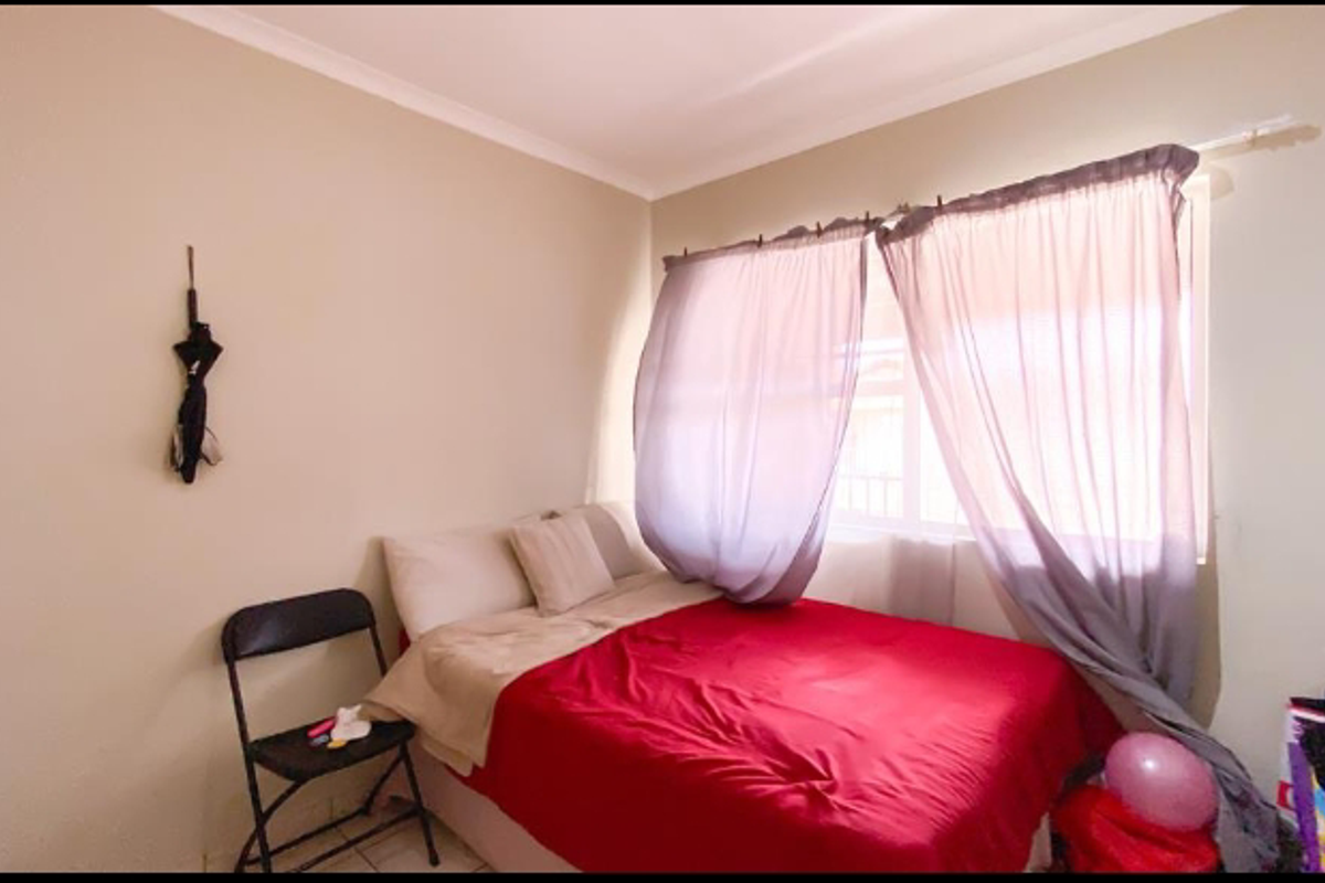 A standard bedroom featuring neutral wall paint, tiled flooring, and a window with curtain tracks.